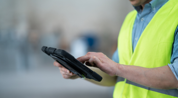 Person in a yellow vest using a tablet in a professional setting.