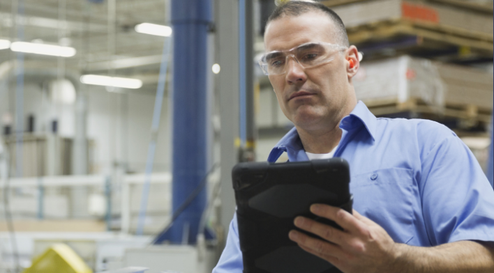 Person in safety glasses using a tablet in an industrial setting.